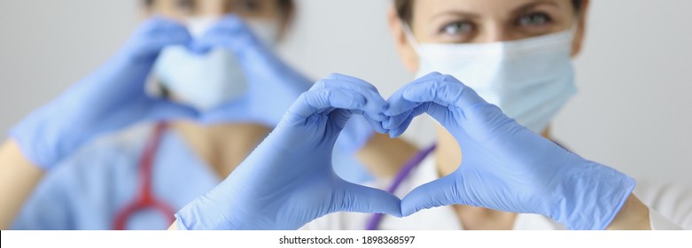Two doctor in medical masks and rubber gloves showing heart with their hands. Treatment of diseases of cardiovascular system concept