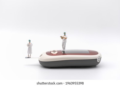 Two Doctor Miniature Figure With Patient File Standing On Glucose Meter On White Background. Using As Diabetes, Glycemia, Health Care And People Concept.