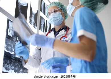 Two Doctor In Suits, Medical Gloves And Protective Masks Hold X-ray Photograph. Two Women Study Results Of Internal Examinations.