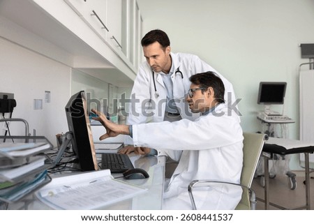 Two doctors engaged in teamwork using computer, discussing patient diagnosis, reviewing medical records, symptoms, and test results, exchanging opinions and knowledge during meeting in consulting room