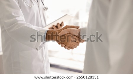 Two doctors in lab coats handshake close up. Male practitioners, medical professionals giving handshake due to cooperation, partnership, working together. Cropped banner shot