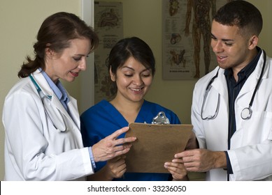 Two Doctors And A Nurse Smiling At The Information They Are Reviewing On A Clipboard.