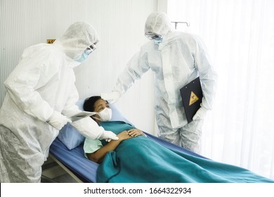 Two Doctors In The Personal Protective Suits Examining The Coronavirus COVID 19 Infected Aging Female Patient In The Control Area. Coronavirus COVID 19 Quarantine Area     