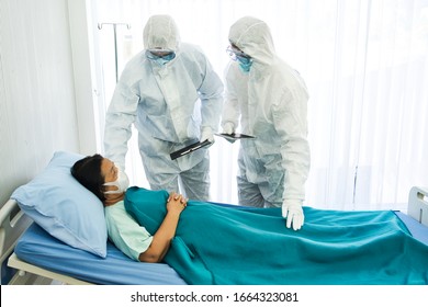 Two doctors in the personal protective suits examining the Coronavirus COVID 19 infected aging female patient in the control area. 