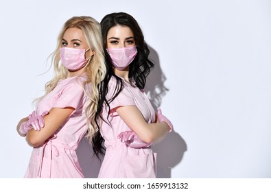 Two Doctors In Pink Scrubs, Disposable Gloves And Medical Masks Are Posing Isolated On White. Medical Staff, Cosmetologist, Tattoo Artist, Hairdresser. Beauty.