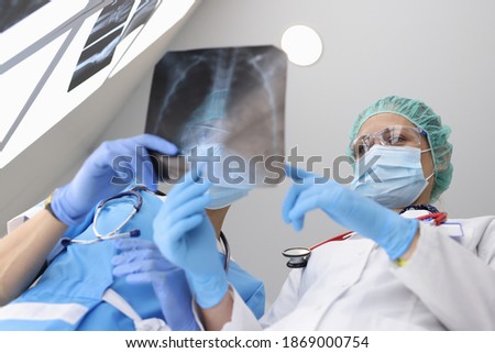 Two doctors in protective mask discuss x-ray of lungs with atypical pneumonia in hospital in covid epidemic. Consultation, diagnosis and treatment of pneumonia.