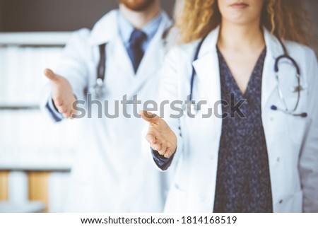 Two doctors standing and offering helping hand for shaking hand or saving life. Medical help, countering viral infection and medicine concept