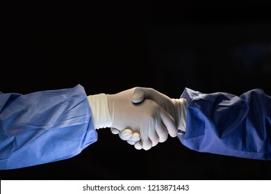 Two Doctors In Surgery Cloth With Rubber Gloves Shaking Hands With Team Confident Before Start To Do Cure Operation In Dark Surgery Room.