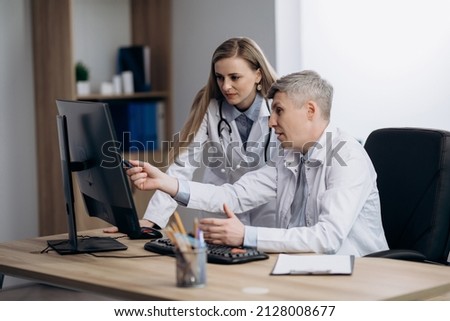 Two doctors talking at workplace looking at computer screen, analyzing results of patients medical examination, feeling satisfied with good news.
