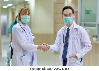 Two Doctors Wear Facial Face Mask And Shake Hand In Hospital Lobby