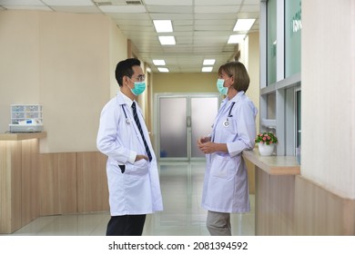 Two Doctors Wearing Protection Facial Mask Are Talking In Hospital Lobby