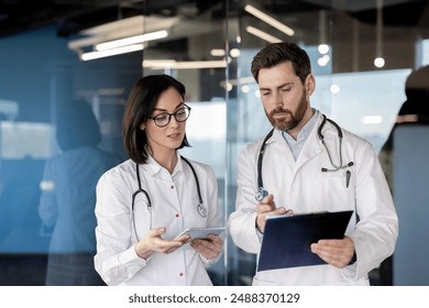 Two doctors in white coats reviewing patient data on a clipboard and tablet in contemporary medical office. Focused healthcare professionals collaborating during work meeting - Powered by Shutterstock