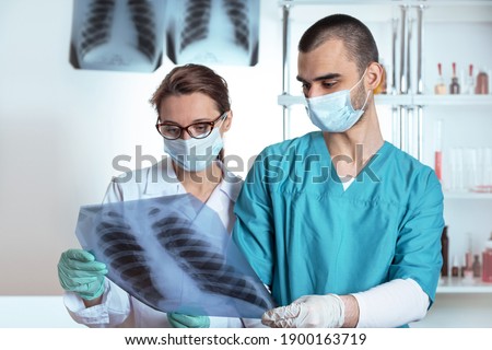 Two doctors woman and man in medical apparel holding x-ray rib cage, lungs, thorax. Lifestyle outdoor scene
