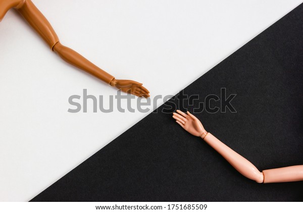 Two doll hands reach for each other on a divided\
black and white background. Stop racism creative concept. Place for\
text, top view, layout
