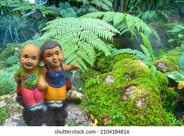 Two Dolls That Look Like Grand Mom  Grand Dad In Asian Uniform Style Sittng On The Rock At Park Background. Father And Mother Concept.