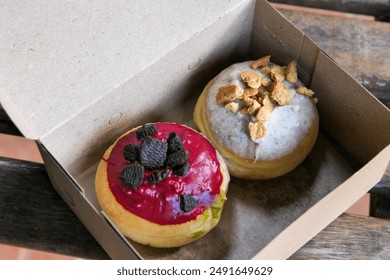 two donuts in a brown packaging box. one red velvet donut with black cookies crumbs and another donut with tiramisu cream and chocolate cookies crumbs