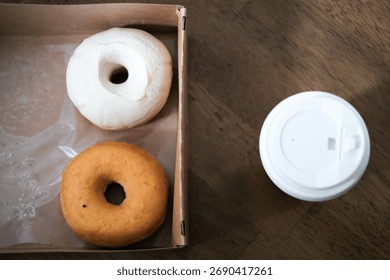 Two donuts left in a box and next to hot coffee cup in the morning.