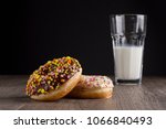 Two donuts lying on the table and on a black background. A glass of milk is next to donuts on a wooden table. Space for text.