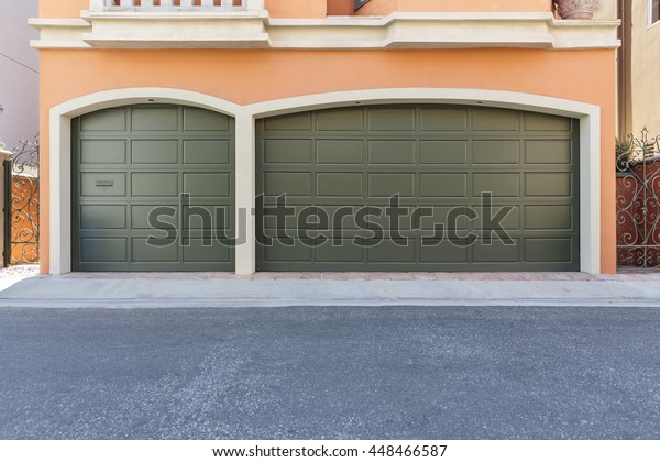 Two door garage door on an empty street in\
a neighborhood.