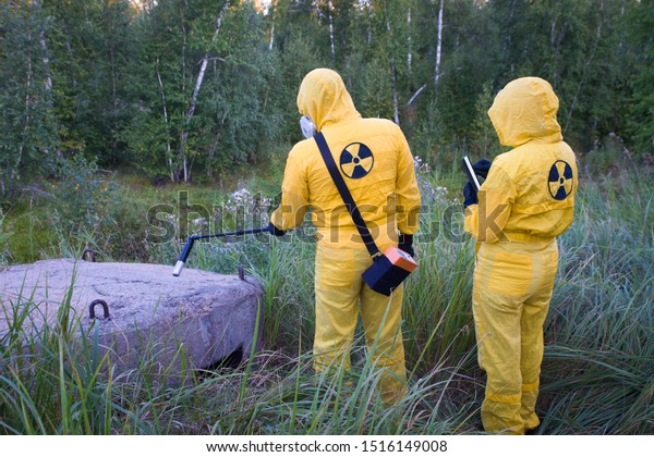 Two dosimetrist \
in protective suite and mask with geiger counter measuring\
radiation level in danger\
zone