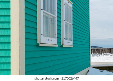 Two double hung windows on a green exterior wall of a vintage style building. The building has narrow horizontal clapboard siding. There's white wooden shutter and trim around the closed glass window. - Powered by Shutterstock