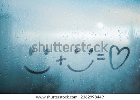 Two drawn smile face and doodle heart on blue foggy glass of window, concept positive photo