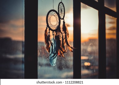 Two dream catchers hanging on the window at sunset time. Boho chic, hope freedom and dream concept.