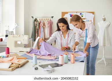 Two dressmakers working together. Seamstresses looking at fabrics. Colleagues discussing quality of textile and production process at modern sewing atelier. Woman teaching coworker a dressmaking trick - Powered by Shutterstock