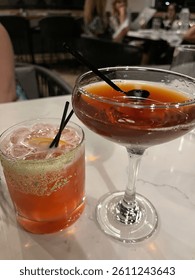 Two drinks, one martini with a cherry and one specialty cocktail 