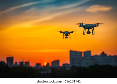 Dos drones cuádruples con una cámara digital de alta resolución volando aérea sobre el espectacular cielo naranja atardecer. La silueta de Cityscape con el sol se cae al fondo.Vehículo al atardecer y espacio de copia