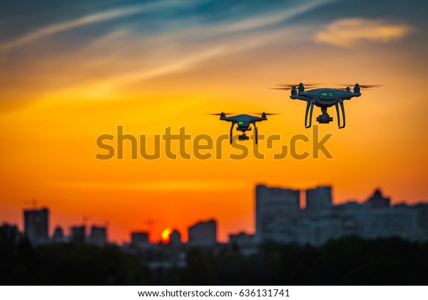 Two drone quad copters with high resolution digital\
camera flying aerial over spectacular sunset orange sky. Cityscape\
silhouette with sun goes down in the background.Vehicle at sundown\
and copy space