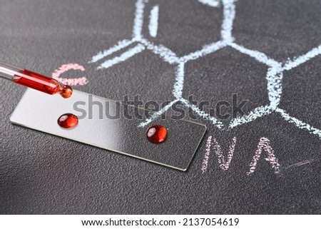 Two drops of red liquid on the  microscope slide and chemical formula on the background.