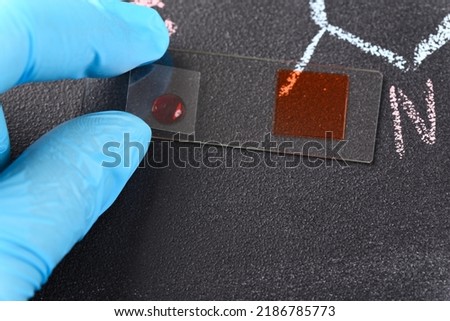 Two drops of red liquid on the  microscope slide and chemical formula on the background.