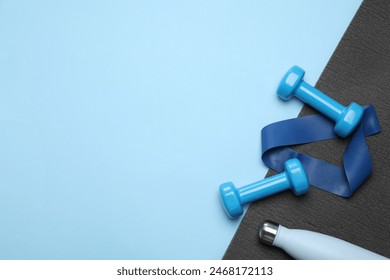 Two dumbbells, yoga mat, fitness elastic band and thermo bottle on light blue background, flat lay. Space for text - Powered by Shutterstock