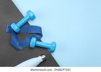 Two dumbbells, yoga mat, fitness elastic band and thermo bottle on light blue background, flat lay. Space for text - Powered by Shutterstock