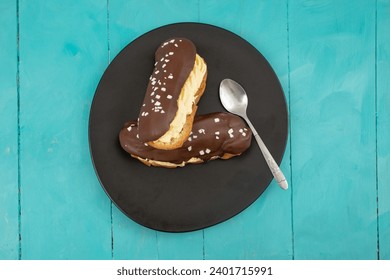 Two eclair cakes on a black ceramic plate, and blue wooden boards table, flat lay