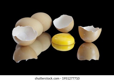 Two eggs acompanied with three empty, broken egg shells and the yellow egg yolk put in the middle, all reflected on the black background