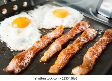 Two Eggs Sunny Side Up And Four Strips Of Bacon Sizzling On Skillet