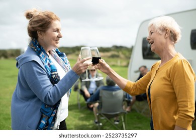 Two elderly Caucasian women enjoying a drink outdoors. Elderly women smiling, holding wine glasses. Outdoor gathering, elderly women, enjoying wine, camper van. Old women drinking wine by camper van - Powered by Shutterstock