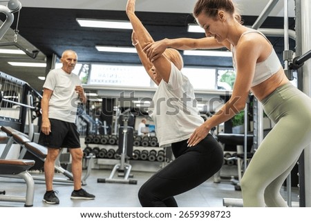 Two elderly couples exercise together with guidance from a young female instructor at the gym, focusing on light workouts and proper technique.