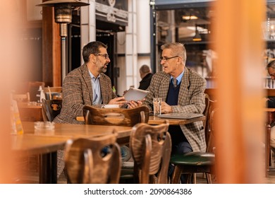 Two elderly handsome businessmen are smiling and looking at the tablet in the café - Powered by Shutterstock