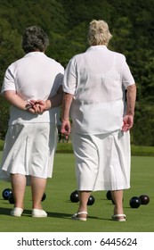 Two Elderly Ladies Dressed In White Outfits,  Standing Together On A Lawn Bowling Green. Rear View.