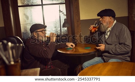 Two elderly men drinking beer at wooden table in rustic atmospheric bar, sharing casual and friendly moment. Concept of elderly people lifestyle, drinks, retro fashion