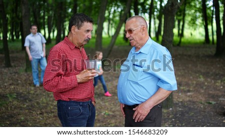 Two elderly people talking in a park. Oldman with plastic cup listening to friend