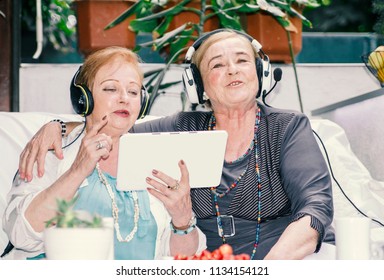 Two Elderly Senior Women Singing Music Using Earphones And Tablet Computer