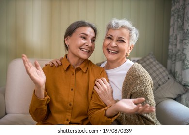Two elderly sisters having fun indoors. Cheerful senior woman enjoying nice time together with her best female friend, sitting on couch at home, laughing, telling jokes. People, aging and friendship