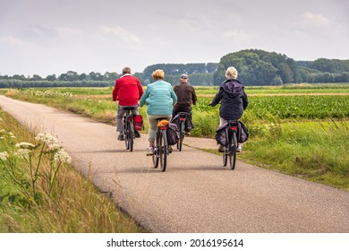 Two elderly unidentified couples with e-bikes cycle on a Dutch country road between fields in the province of North Brabant. The photo was taken on a slightly cloudy day in the summer season.