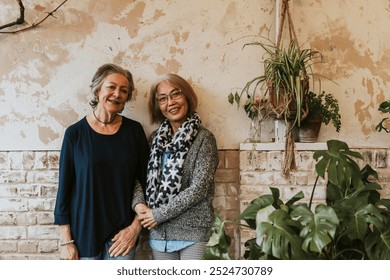 Two elderly women, Asian and Caucasian, smiling together. Happy elderly women are standing in front of a rustic wall with plants. Happy senior women enjoying with plants. Friendship - Powered by Shutterstock