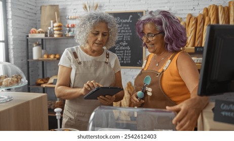 Two elderly women bakers working together in a cozy bakery interior, with one using a tablet and the other smiling beside bakery goods. - Powered by Shutterstock