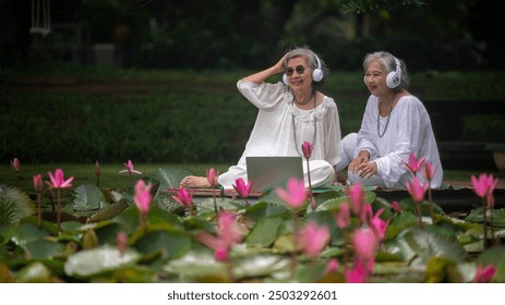 Two elderly women enjoying a nature setting listen music ,eating fresh focusing a plant lotus in the greenery around them is elder lifestyle concept. - Powered by Shutterstock